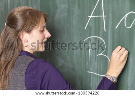 Teacher in front of a blackboard at school. She is writing some letters to blackboard.