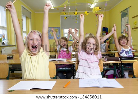 Children in a yellow classroom. They all raises up the hands.