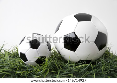 Picture shows two footballs on a green field. Tabletop with white background