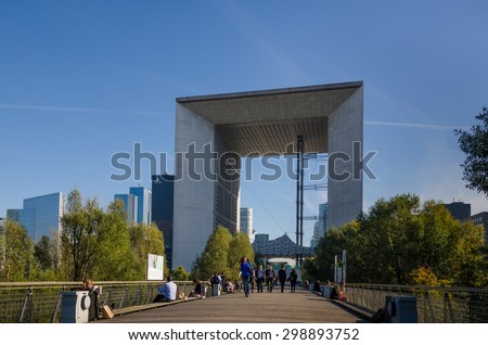 PARIS, FRANCE - OCTOBER 27, 2014: People walk along La Jetee, a boardwalk behind La Grande Arche  in in La Defense, where employees are sitting along the fence eating their lunch.