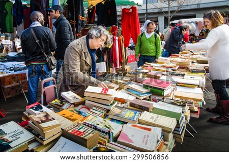 PARIS, FRANCE - OCTOBER 5, 2014: Women check the table of used books at a flea market in the historic Marche d\' Aligre in the Bastille district.
