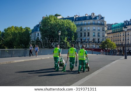 PARIS, FRANCE - AUGUST 22, 2015:  Sanitation workers cross the St. Louis Bridge to  St. Louis Island with their carts on a sunny, summer day to clean the streets of this popular tourist destination.