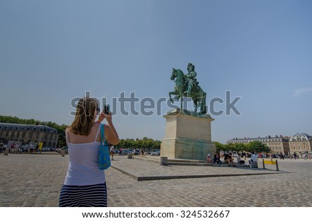 PARIS, FRANCE - AUGUST 12, 2015: Tourist takes a photo of a statue of the Sun King Louis XIV on his horse in the Place dâ??Armes in front of the Palace of Versailles.