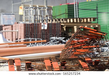 A pile of building materials lies  on the ground  on a building  site waiting for demolition of the old building to be completed before construction begins.