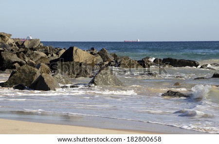 Indian ocean waves rolling in on the rocks on the sandy  beach near a  rocky groyne  by the  land backed harbour in Bunbury south western Australia on a fine autumn morning.