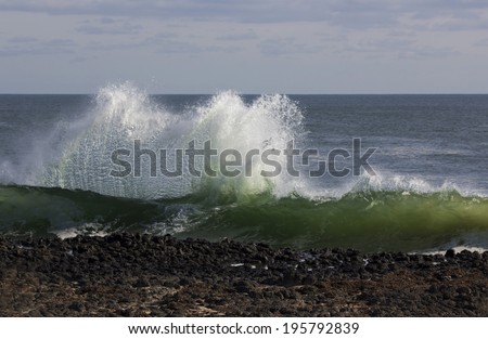 Indian Ocean waves breaking on basalt rocks at  Ocean beach Bunbury Western Australia on a cloudy afternoon in late autumn  send salty spray high into the air.