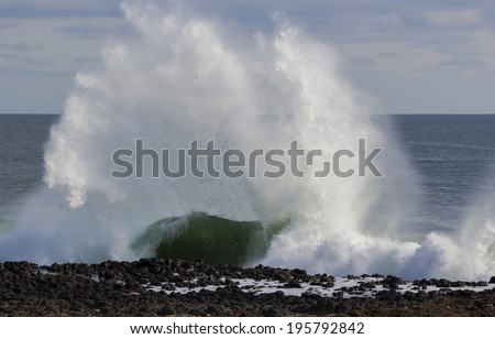 Indian Ocean waves breaking on basalt rocks at  Ocean beach Bunbury Western Australia on a cloudy afternoon in late autumn  send salty spray high into the air.