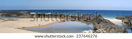 Panorama of  the calm Indian Ocean waves breaking on grey weathered  basalt rocks at  Ocean beach Bunbury Western Australia on a fine sunny  morning in early  summer are cool and refreshing.