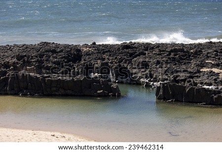 The calm Indian Ocean waves breaking on grey weathered  basalt rocks at  Ocean beach Bunbury Western Australia on a fine sunny  morning in early  summer are cool and refreshing.