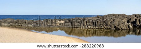 Panorama of  the calm Indian Ocean waves breaking on grey weathered  basalt rocks at  Ocean beach Bunbury Western Australia on a fine sunny  morning in mid   summer are cool and refreshing.