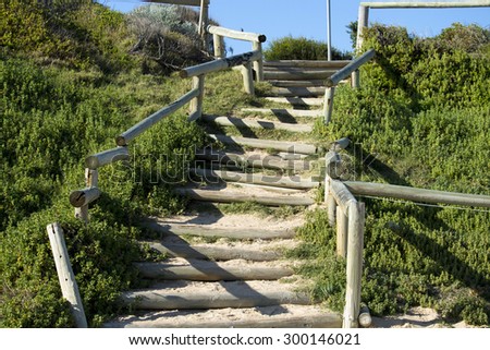 Wooden  pole steps with green vegetation on either side  leading down to the ocean at Ocean Beach Bunbury Western Australia on a calm   sunny  winter morning.