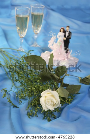 a photo of wedding cake dolls, rose and glasses over blue