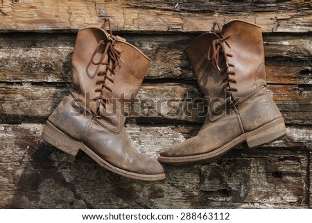 Two old boots hanging on a wooden wall.
