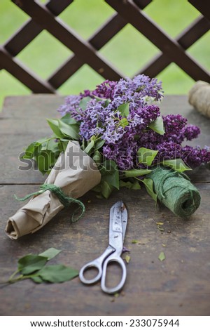 Lilacs bouquet wrapped in craft paper, green twine and scissors on wooden table