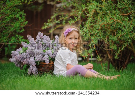 cute child girl plays in spring garden with basket of lilacs