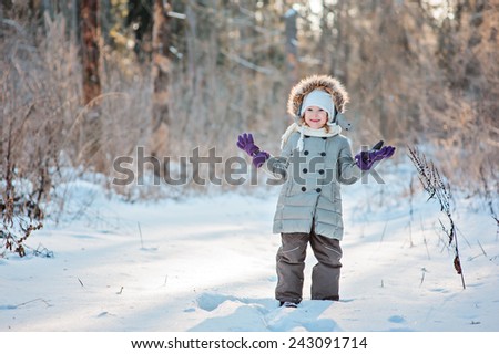 portrait of cute happy child girl looking at camera in sunny winter forest