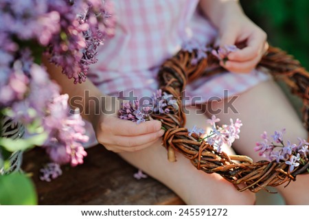 close up of little girl hands making lilac wreath in spring garden