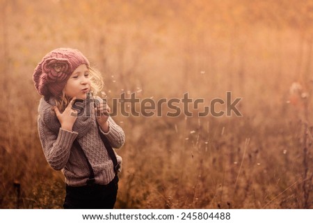 adorable child girl in pink knitted hat blowing dandelion autumn portrait in vintage pastele tones