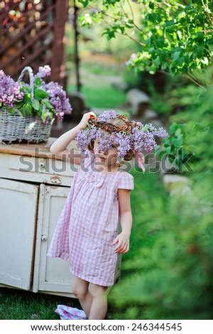 cute child girl in pink plaid dress playing with lilac wreath in spring garden