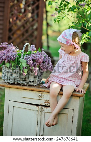 adorable child girl in pink plaid dress with basket of lilacs in spring garden
