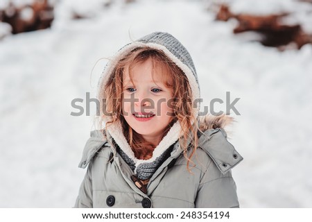 winter outdoor portrait of cute smiling child girl in grey coat on the walk in snowy forest