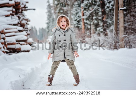 Funny happy child girl on the walk in winter forest with tree felling on background