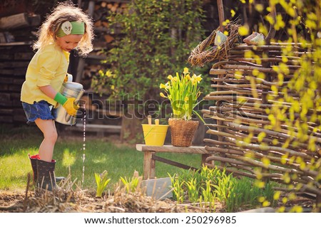 child girl in yellow cardigan watering flowers in spring garden