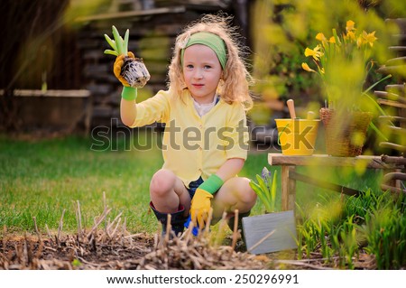 child girl in yellow cardigan planting flowers in spring garden