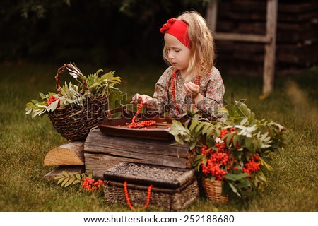 cute child girl making rowan berry beads in autumn garden