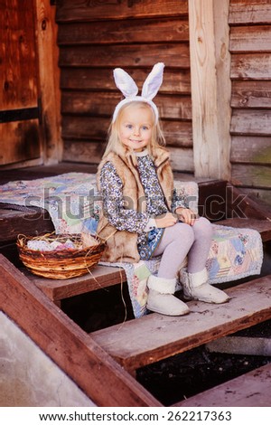 cute smiling child girl wearing bunny ears for easter sitting at country house