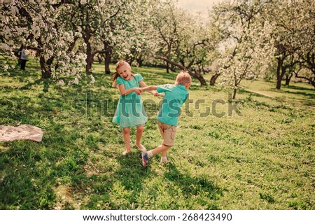 happy brother and sister are dancing in spring apple garden