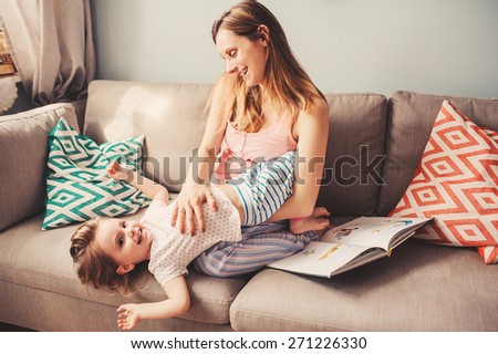 happy toddler girl playing with mother at home on the sofa