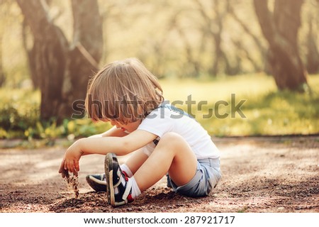 toddler boy playing with sand on the ground in spring