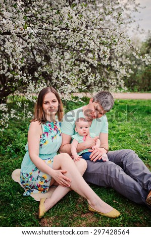 happy family sitting under the tree on the walk with baby daughter in blooming spring park