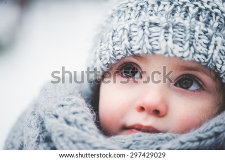 winter close up outdoor portrait of adorable dreamy baby girl in grey knitted hat and scarf