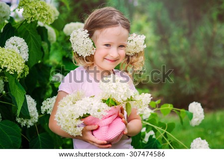smiling child girl with hydrangea bouquet in summer garden near flowering bush