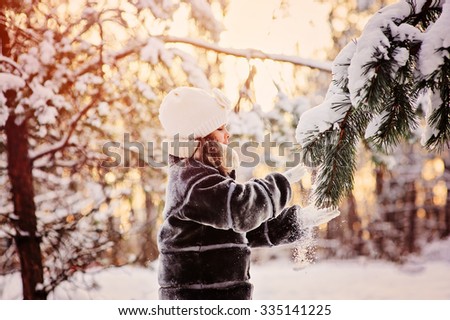 child girl playing with snow on winter forest walk. Cozy mood, seasonal outdoor activities.