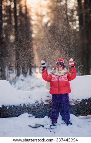 happy toddler girl drops snow on the walk in snowy winter forest,  outdoor cozy christmas holidays