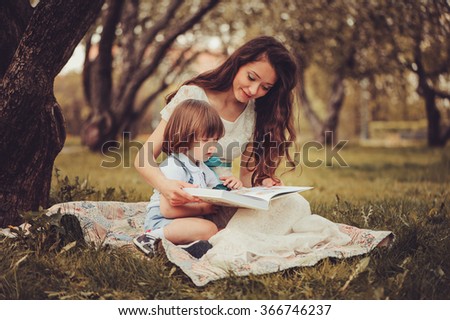 mother reading book to toddler son outdoor in spring garden. Family spending time together on picnic. Parent teaching kids on summer vacation.