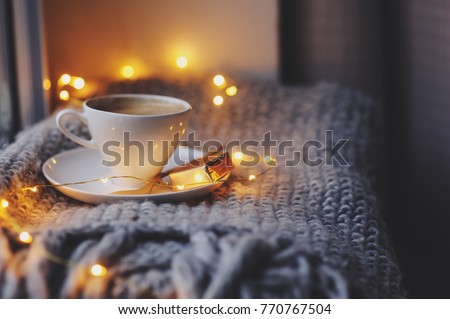 cozy winter or autumn morning at home. Hot coffee with gold metallic spoon, warm blanket, garland and candle lights, swedish hygge concept.