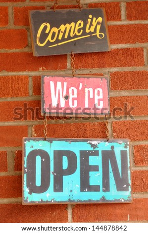 Antique Come in We're Open Sign Hanging on a Brick Wall
