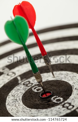 Two darts on a dartboard. One in the center, bulls eye the other off center.