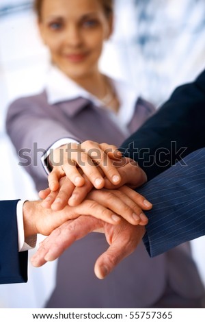 A group of business people making a pile of hands with a woman at the background.