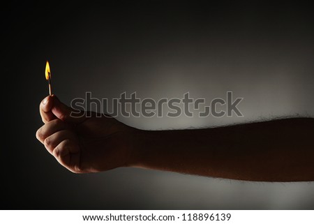 Hand holding burning match against dark background.