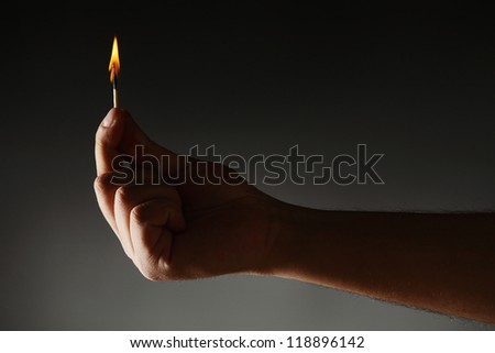 Hand holding burning match against dark background.