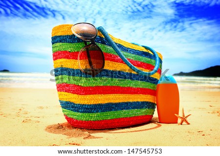 Colorful straw bag, sunglasses, bottle of sun lotion and starfish on paradise tropical beach