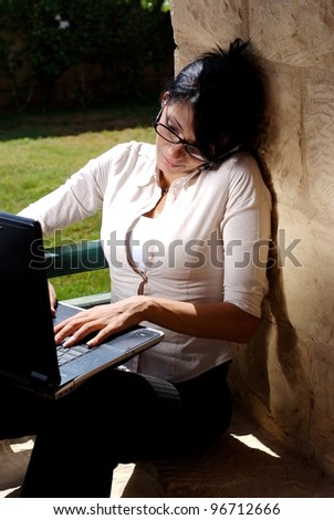 A female working on a lap top in a garden space and talking on a mobile phone