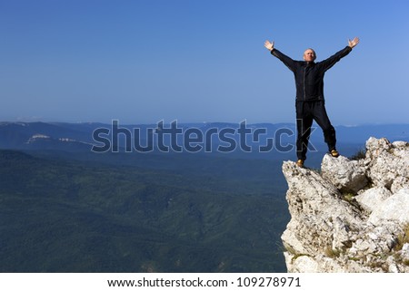The man in a jumpsuit costs on the rock in mountains, having lifted up hands