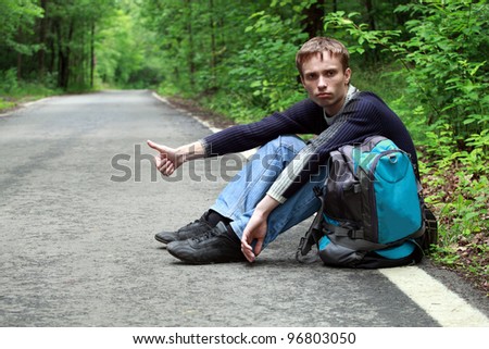 The young guy in jeans and a sweater stops the car on road, sitting on a roadside and having lifted a finger upwards
