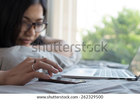 Asian girl is enjoying her cell phone on a bed in her vacation at her house.